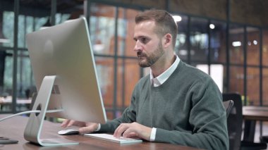 Genç adam ofiste bilgisayarla çalışıyor.