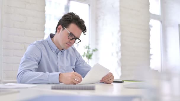 Привлекательный рабочий молодой человек читает документы в офисе — стоковое видео