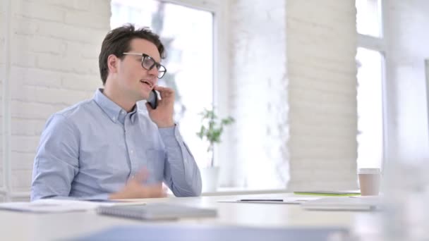 Joven trabajador enojado hablando en el teléfono inteligente en la oficina — Vídeos de Stock