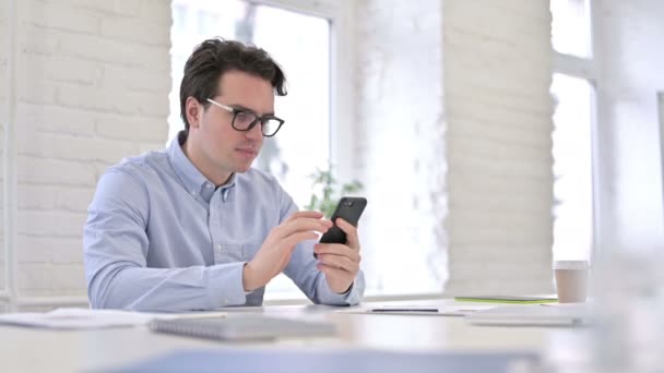 Atractivo joven trabajador que habla en el teléfono inteligente en la oficina — Vídeos de Stock