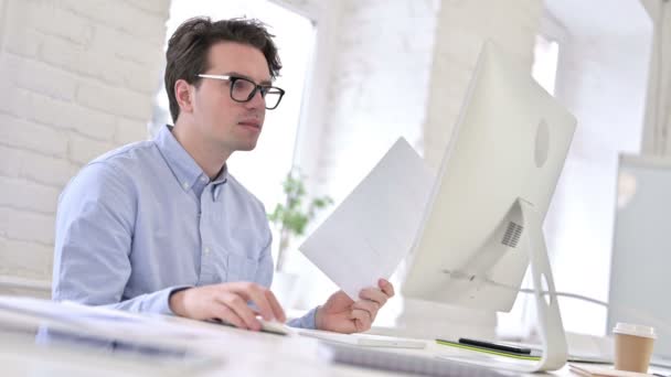 Çalışan Genç Adam Belgeleri Okuyor ve Ofiste Dizüstü bilgisayar kullanıyor — Stok video