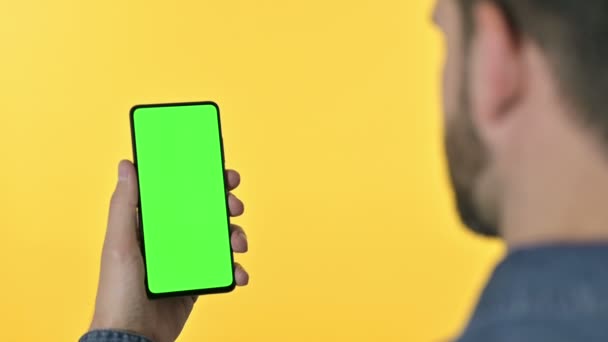 Mann scrollt Smartphone mit Chroma-Bildschirm, gelber Hintergrund — Stockvideo