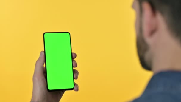 Designer op zoek naar Smartphone met chroma scherm, gele achtergrond — Stockvideo