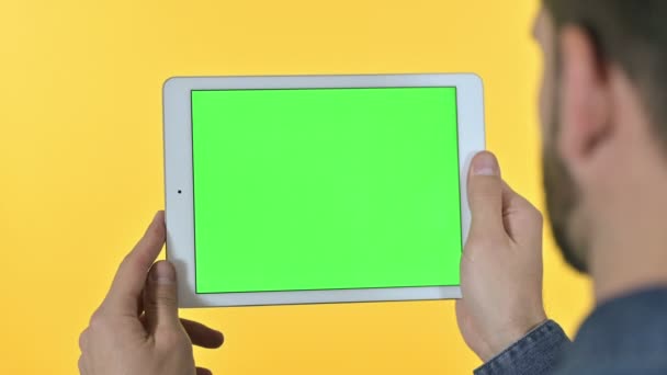 Mann blättert auf Tablet mit Chroma-Bildschirm, gelber Hintergrund — Stockvideo