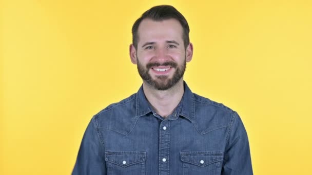 Junger Mann mit Bart winkt in die Kamera, gelber Hintergrund — Stockvideo