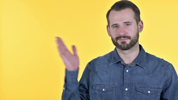 Baard jongeman houden van product op hand, gele achtergrond — Stockvideo