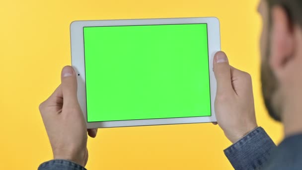 Man op zoek naar tablet met chroma scherm, gele achtergrond — Stockvideo