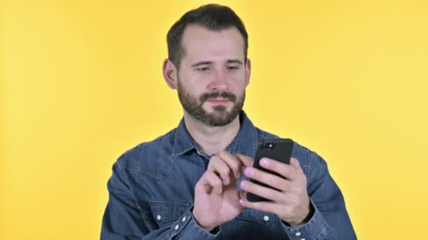 Homem jovem barba usando Smartphone, fundo amarelo — Vídeo de Stock