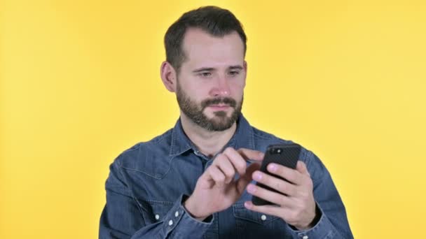 Barba joven celebrando el éxito en el teléfono inteligente, fondo amarillo — Vídeos de Stock