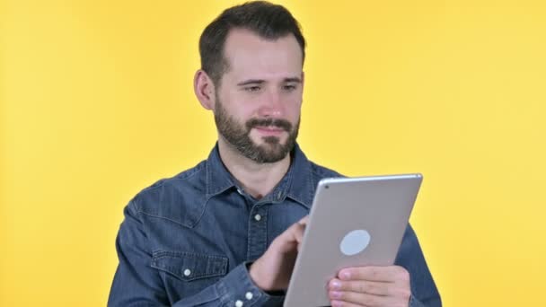 Hardwerkende baard jongeman met behulp van tablet, gele achtergrond — Stockvideo