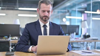 Ofis masasında dizüstü bilgisayarda çalışan genç iş adamı.