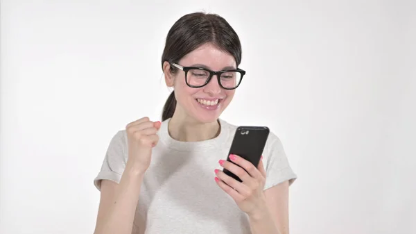 A jovem mulher excitada olhando para o telefone e celebrando em fundo branco — Fotografia de Stock