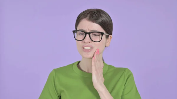 Хвороблива молода жінка має зубний біль на фіолетовому фоні — стокове фото