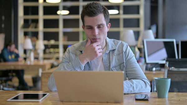 The Serious Young Male Designer Thinking and working on Laptop