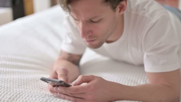 Сфокусированный молодой человек с помощью смартфона в постели — стоковое видео