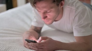 Yatakta akıllı telefon kullanan yakışıklı genç adam. 