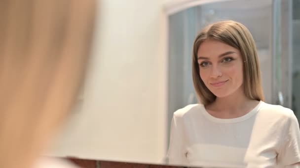 Achteraanzicht van een jonge vrouw die in de spiegel kijkt en glimlacht — Stockvideo