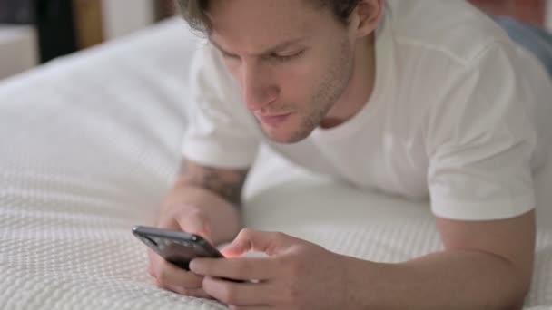 Fešák mladý muž pomocí Smartphone v posteli — Stock video