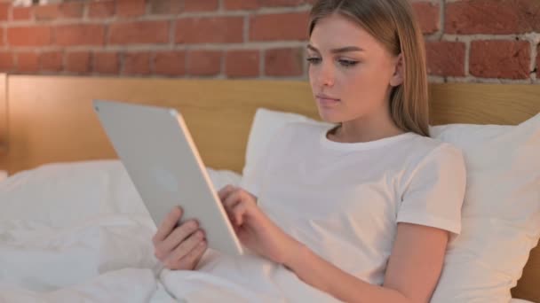 Mujer joven decepcionada reaccionando a la pérdida en la tableta en la cama — Vídeo de stock