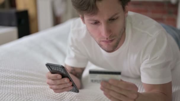 Homem jovem usando cartão de crédito no Smartphone na cama — Vídeo de Stock