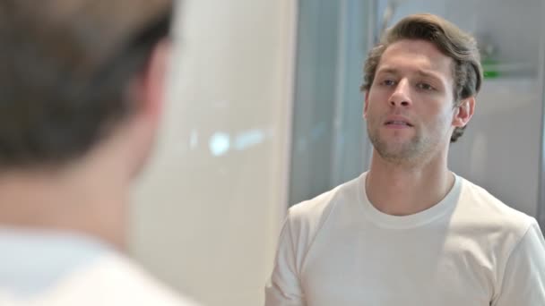 Вид сзади расстроенного молодого человека, смотрящего на себя в зеркало — стоковое видео