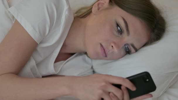 Portret młodej kobiety w szoku przy użyciu smartfona w łóżku — Wideo stockowe