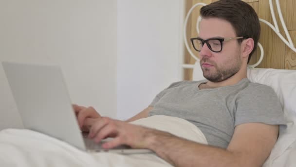 Vousy mladý muž pracující na notebooku v posteli — Stock video
