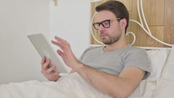 Ambicioso barba joven hombre usando tableta en cama — Vídeos de Stock