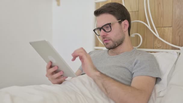 Rozrušený vousy mladý muž dostat šok na tabletu v posteli — Stock video