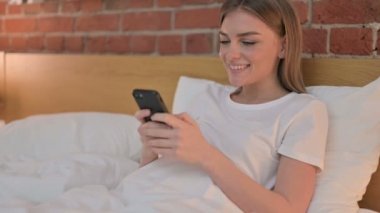 Yatakta akıllı telefon kullanan çekici genç kadın. 