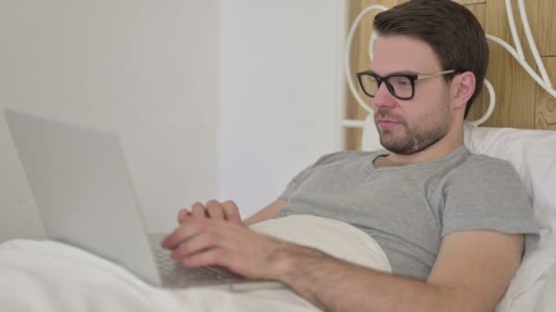 Barba Joven haciendo Video Chat en el ordenador portátil en la cama — Vídeos de Stock