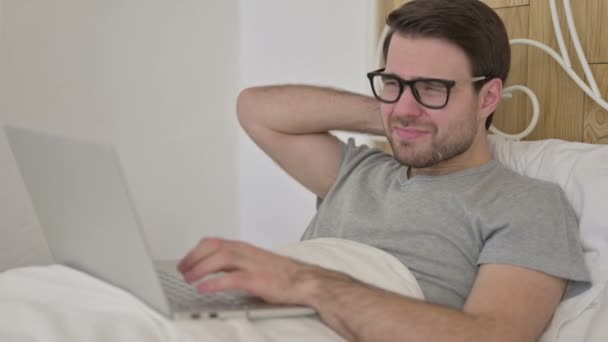 Baard jongeman met nekpijn op laptop in bed — Stockvideo