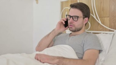 Üzgün Sakallı Genç Adam Yatakta Akıllı Telefonla Konuşuyor