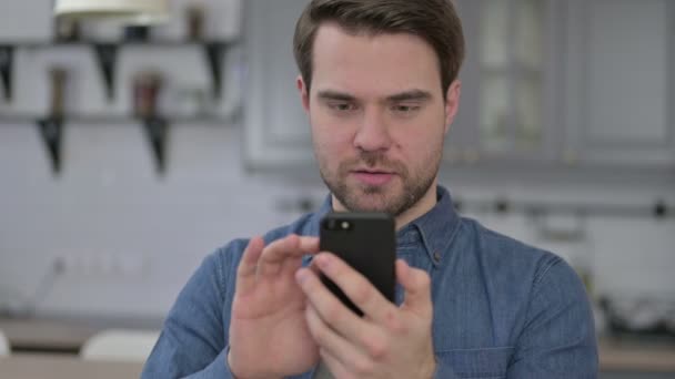 Портрет молодого человека с бородой, празднующего успех на смартфоне — стоковое видео