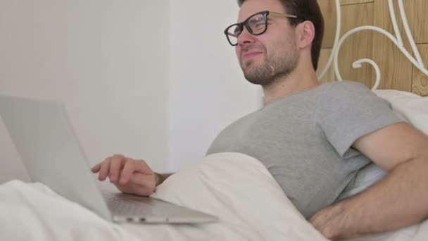 Barba joven con dolor de espalda en el ordenador portátil en la cama — Vídeos de Stock
