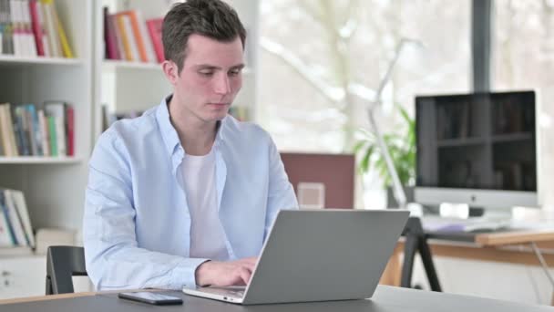 Jovem trabalhando no laptop olhando para a câmera — Vídeo de Stock