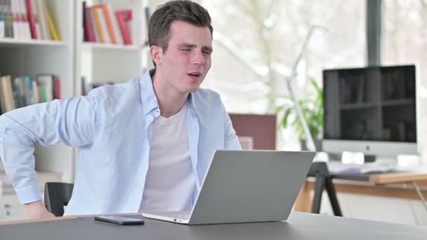 Junger Mann mit Rückenschmerzen arbeitet am Laptop — Stockvideo