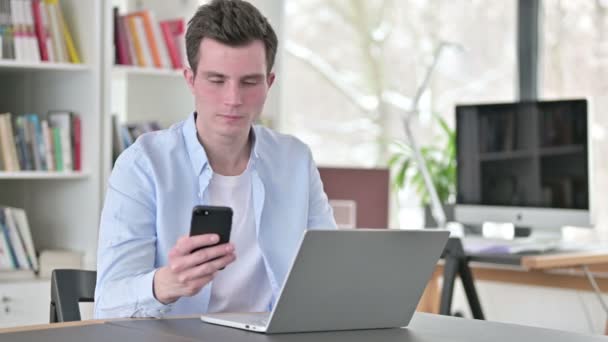 Jonge man werkt op laptop en het gebruik van Smartphone — Stockvideo
