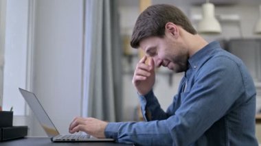 Sakallı genç adamın dizüstü bilgisayarında baş ağrısı var.