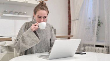 Genç bir kadının kahvesini içip laptopla uğraşması.