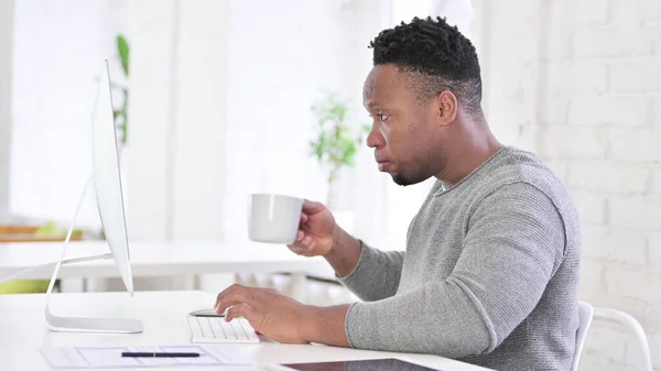 Hombre africano bebiendo café y trabajando en el escritorio —  Fotos de Stock
