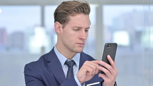 Portret van Vrolijke jonge zakenman met behulp van Smartphone in Office — Stockfoto