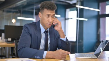 Genç İşadamı Akıllı Telefonla Konuşuyor ve Bilgisayarda Çalışıyor