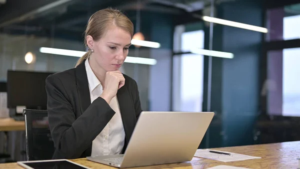 Молодая предпринимательница думает и работает над ноутбуком в офисе — стоковое фото
