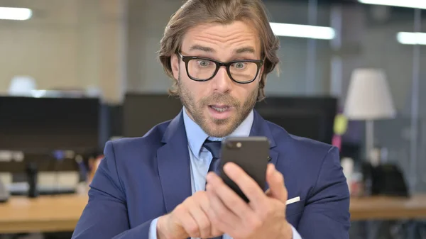 Empresario en shock mirando la pantalla del teléfono inteligente — Foto de Stock