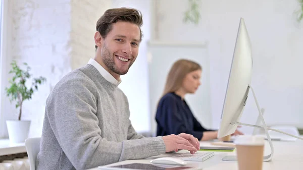 Joven trabajando en el escritorio y sonriendo a la cámara — Foto de Stock