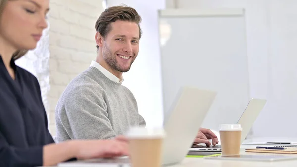 Hombre joven trabajando en el ordenador portátil y sonriendo a la cámara — Foto de Stock