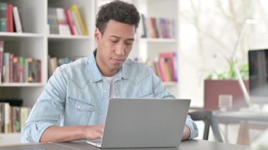 Young African American Man Smiling at Camera while Working on Laptop 
