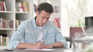Young African American Man Writing on Paper at Work 