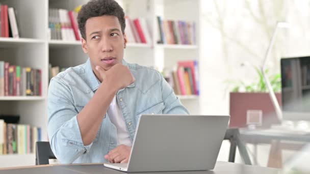 Hombre joven afroamericano que piensa y trabaja en el ordenador portátil, lluvia de ideas — Vídeo de stock